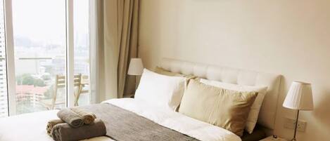 A hotel room with a large bed, a view of the city, and a window with curtains.