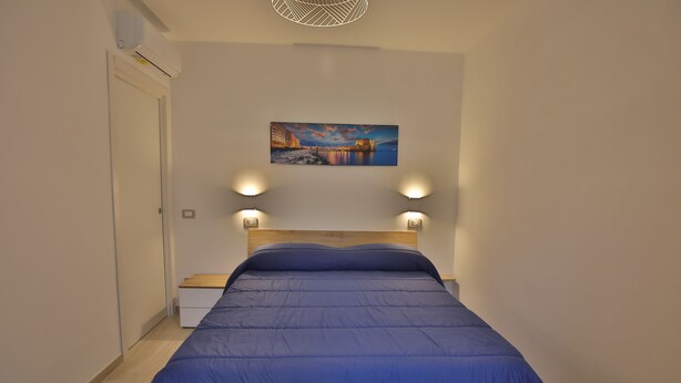 A bedroom with a bed, a nightstand, a wall-mounted painting, and two wall-mounted lights. - 1 Bedroom Apartment in Castellammare di Stabia (Castellammare di Stabia)