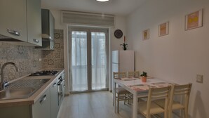 A modern kitchen with a sink, stove, and cabinets, leading to a dining area with a table and chairs. - 1 Bedroom Apartment in Castellammare di Stabia (Castellammare di Stabia)