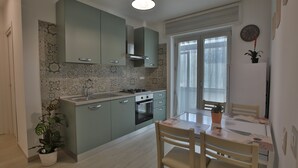 A modern kitchen with light green cabinets, a white countertop, and a dining area with a table and chairs. - 1 Bedroom Apartment in Castellammare di Stabia (Castellammare di Stabia)