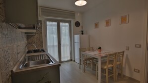 A kitchen with a sink, stove, and dining table with chairs. There is a refrigerator and a window with curtains. - 1 Bedroom Apartment in Castellammare di Stabia (Castellammare di Stabia)