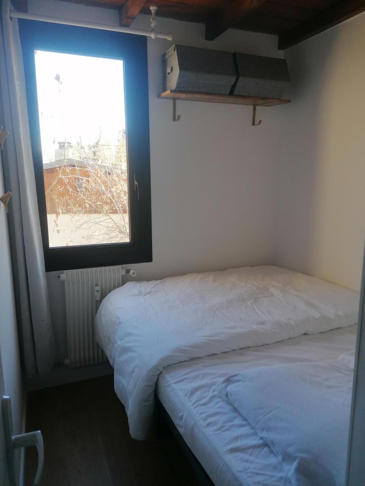 A small, single-bed room with a window, a radiator, and a wooden ceiling.