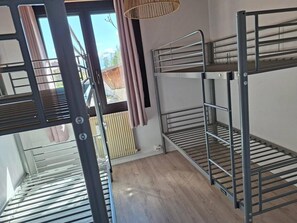 A bunk bed room with a view of the outdoors, a window with curtains, and a radiator.
