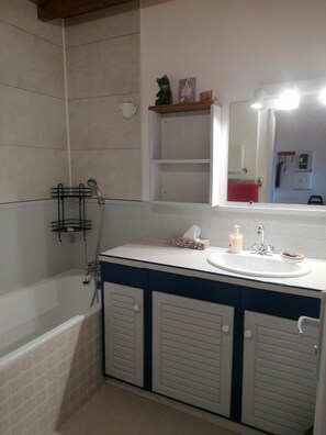 A bathroom with a bathtub, a sink with a mirror, and a shelf above the mirror.