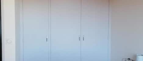 A bedroom with a large wardrobe, a bed with white bedding, and a wooden ceiling.