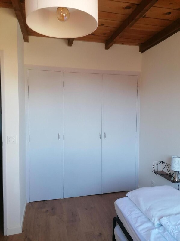 A bedroom with a large wardrobe, a bed with white bedding, and a wooden ceiling.