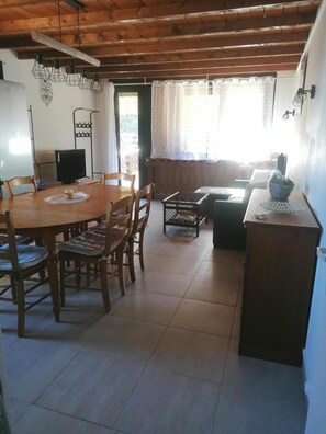 A dining area with a wooden table and chairs, a television, and a kitchen area with a refrigerator.
