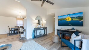 A modern living room with a fireplace, a dining area, and a large TV displaying a scenic view.