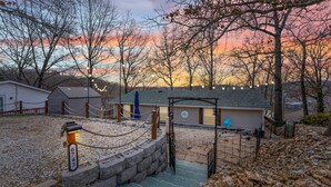 A rustic cabin with a stone entrance, surrounded by trees and a sunset view.