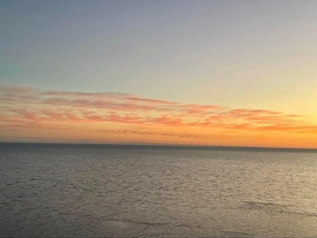 A calm sea at sunset with a clear sky.