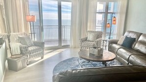 Un salon spacieux avec un canapé en cuir, deux fauteuils, une table basse et une vue sur la mer grâce à de grandes fenêtres.