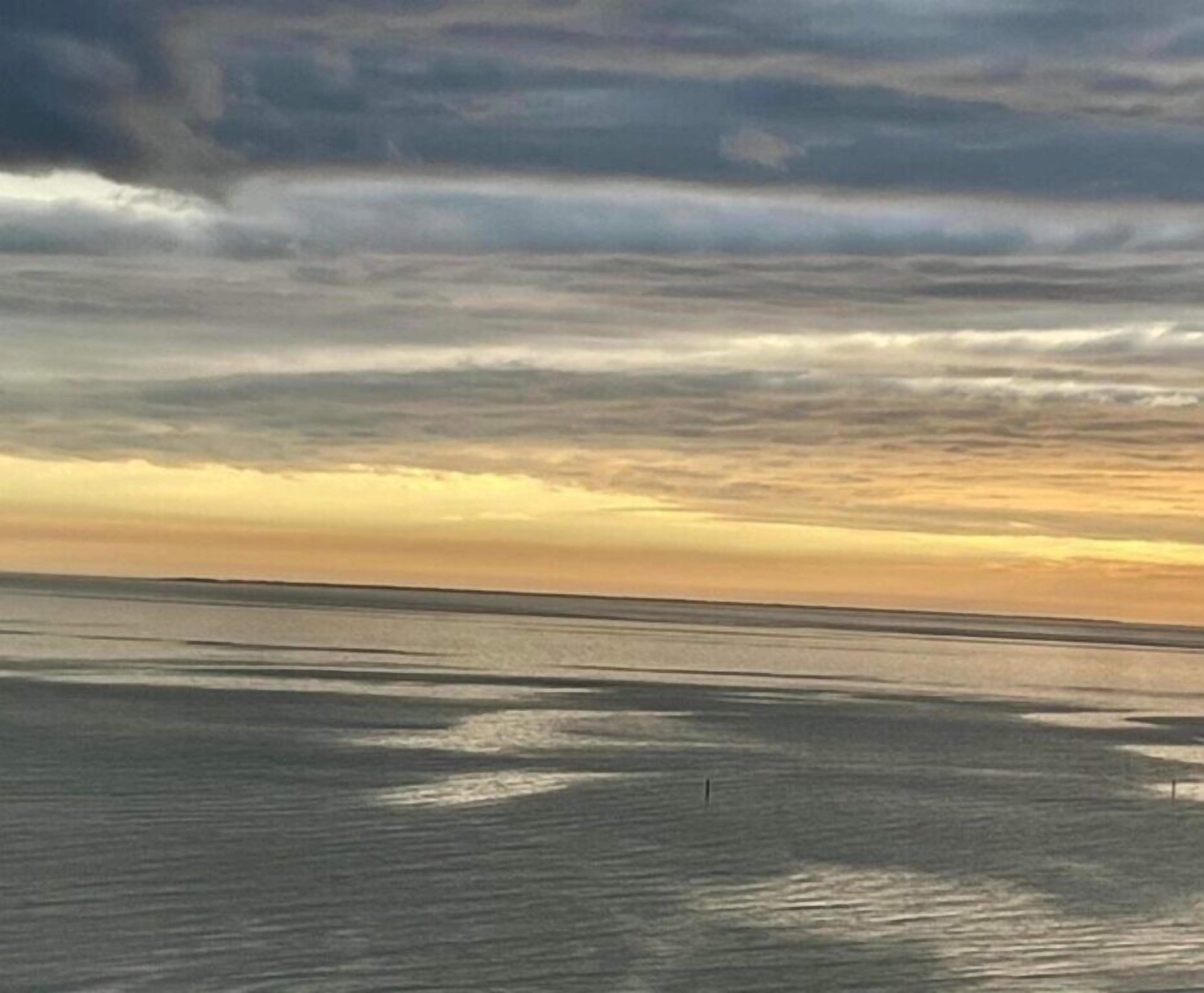 Une plage avec une mer calme et un ciel nuageux.