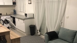 Un espacio habitable compacto con kitchenette, un sofá, una pequeña mesa y una lavadora.