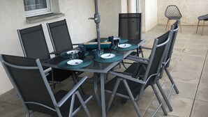 Un patio con mesa lista para cuatro personas, rodeada de sillas y cubierta por una sombrilla grande.