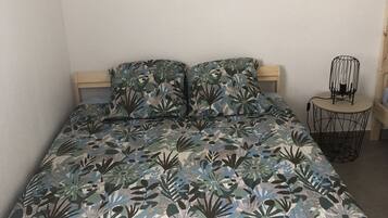 Quarto com colcha estampada de flores, cabeceira de madeira e dois letreiros fixados na parede com texto em francês.