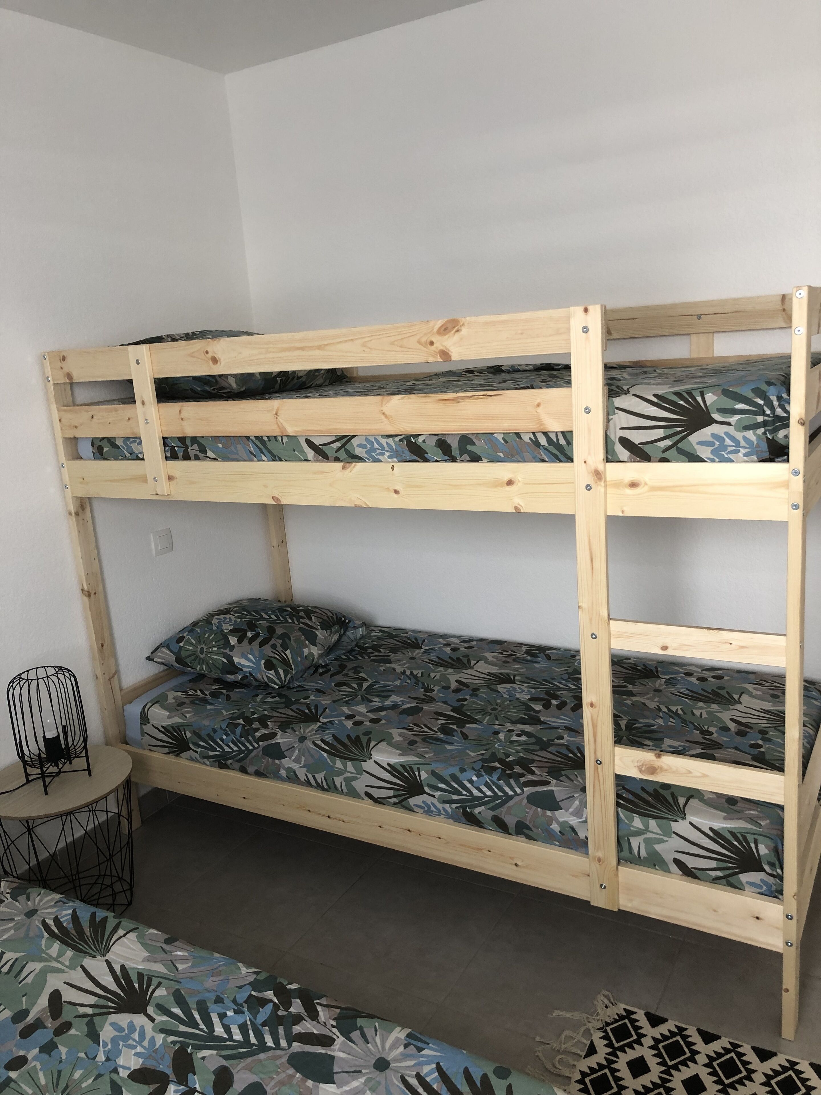A bunk bed with a camouflage-patterned mattress and a small round table with a black metal frame.