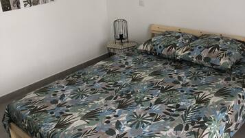 A bed with a floral bedspread, a small table with a chair, and a wall-mounted photo collage.
