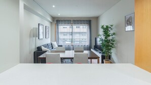 Et moderne, lyst rum med spisebord, stole, sofa, fjernsyn og en potteplante.