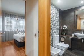 Une chambre d’hôtel moderne équipée d’un lit, d’une salle de bain avec un lavabo, des toilettes et un bidet, ainsi que d’un grand miroir.