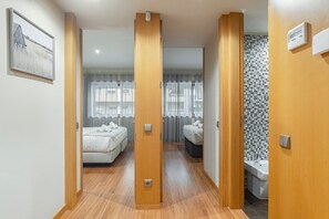Une chambre d’hôtel avec un plancher en bois, un lit avec une literie blanche, une salle de bain avec un mur de douche carrelé et un tableau accroché au mur.