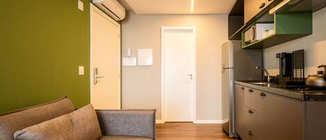 Cocina compacta con horno integrado, microondas y refrigerador de acero inoxidable. Piso de madera y pared verde.