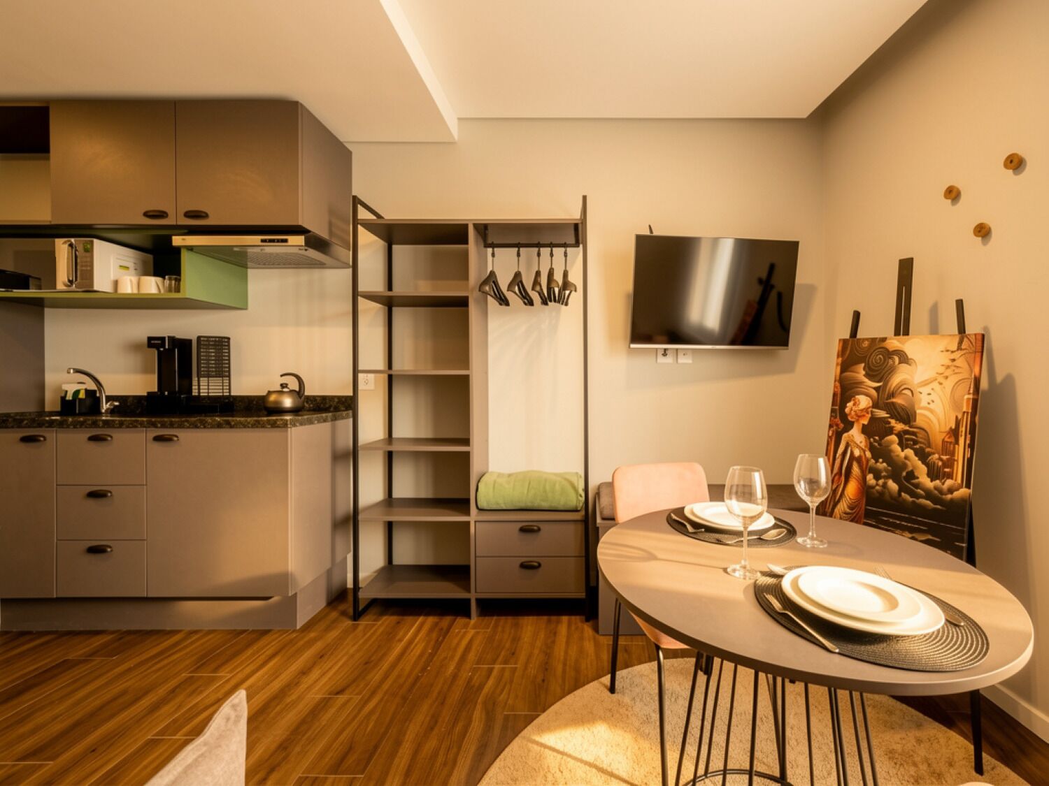 A modern kitchen with a dining area, a TV mounted on the wall, and a painting on the wall.
