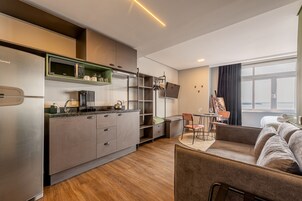 Una cocina moderna con un refrigerador empotrado, una cafetera y un hervidor. Hay un comedor con una mesa y sillas, y un sofá en la sala de estar.