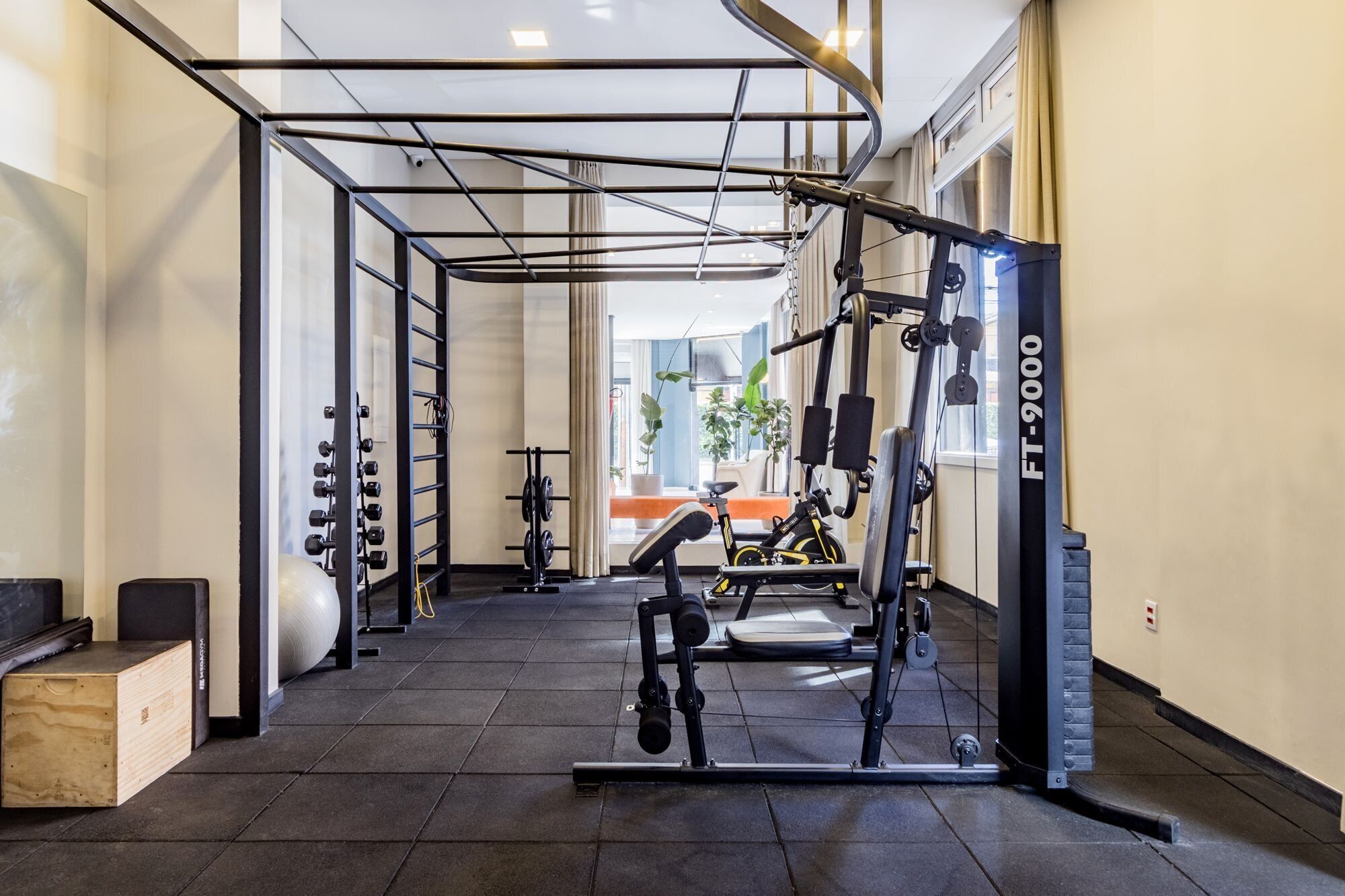 Une salle de sport équipée de matériel d’exercice, d’une barre de traction et d’une fenêtre avec des rideaux.