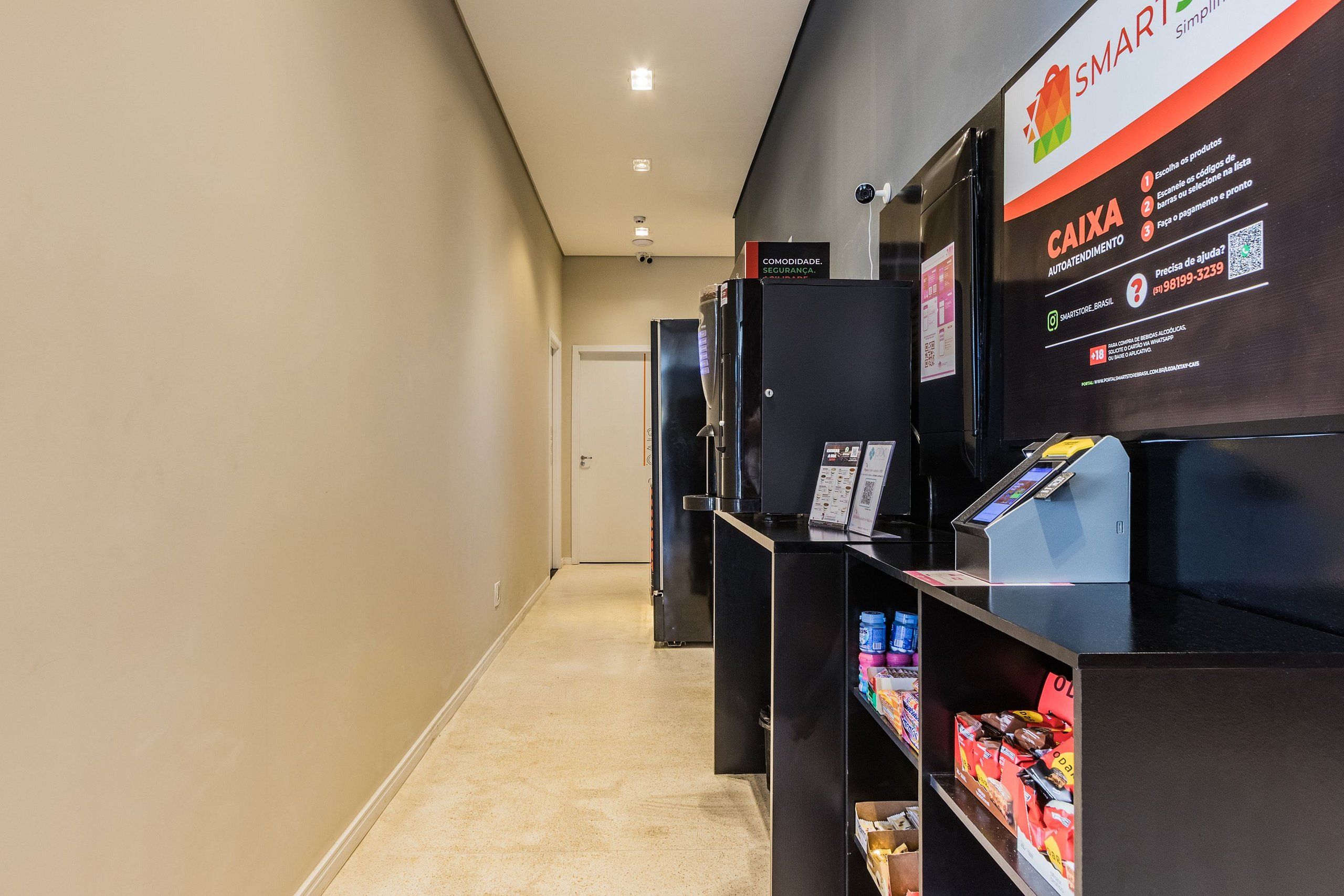 A corridor with a self-service kiosk and shelves stocked with snacks.