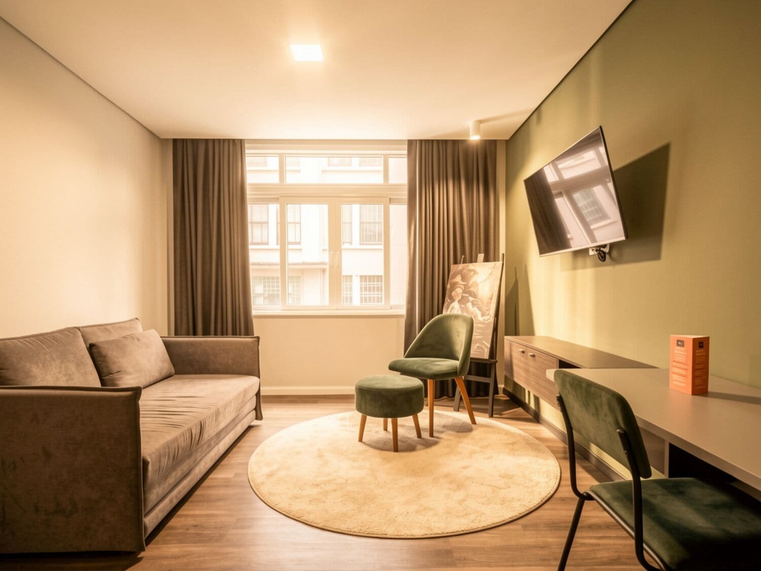 Una sala de estar moderna con un sofá, dos sillones, una mesita, un televisor montado en la pared y una ventana con cortinas.
