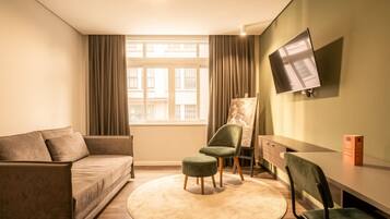 Una sala de estar moderna con un sofá, dos sillones, una mesita, un televisor montado en la pared y una ventana con cortinas.