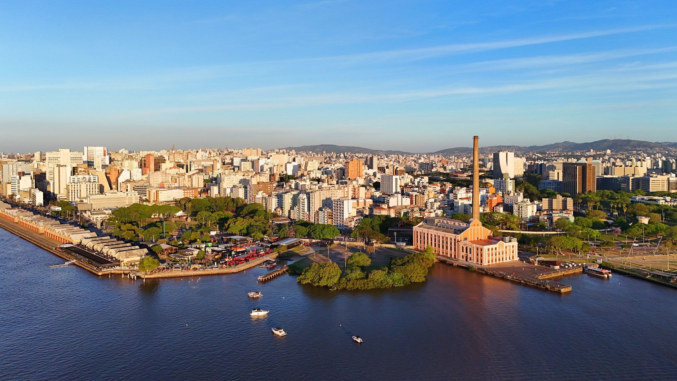 Un paysage urbain caractérisé par une rivière imposante, un grand bâtiment industriel doté d’une haute cheminée, et une urbanisation dense.
