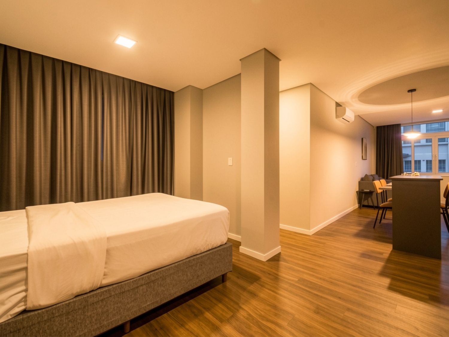 Habitación de hotel moderna con una cama grande, una pequeña cocina y vistas a la ciudad.