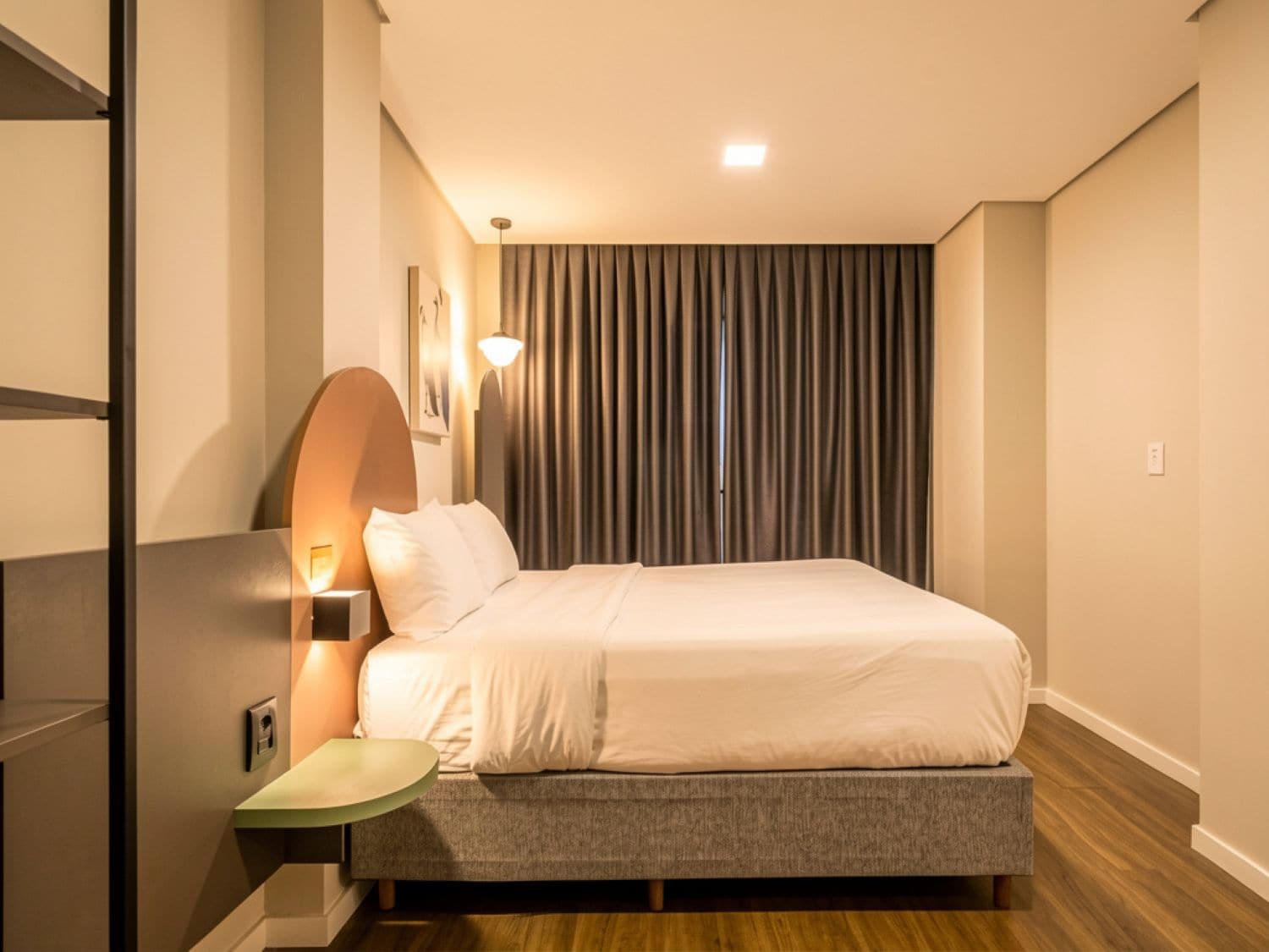 A modern bedroom with a bed, a nightstand, a wall-mounted lamp, and a window with curtains.