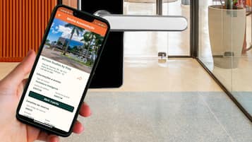 A smartphone displaying a hotel booking interface with a view of a modern lobby, including a reception desk, a chair, and a potted plant.