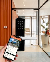 Un teléfono inteligente muestra una interfaz de reserva de hotel con vista a un vestíbulo moderno, que incluye un mostrador de recepción, una silla y una planta en maceta.