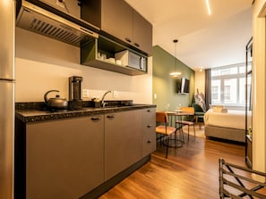 A modern kitchen with a built-in stove, a coffee maker, and a microwave. There is a dining area with a table and chairs, and a bed in the adjacent room. - Xtay Porto Alegre Cais Rooftop (Porto Alegre)