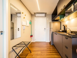 A modern kitchen with a built-in oven, a microwave, and a sink. There is a broom leaning against the wall and a small table with a kettle.