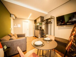 A modern living room with a sofa, a dining table set for two, and a kitchen area with a refrigerator and cabinets.
