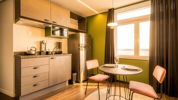 Una cocina compacta con electrodomésticos modernos, un comedor con dos sillas y vistas a través de una ventana con cortinas.