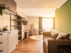 A modern living room with a sofa, a dining area with a table and chairs, and a kitchen with cabinets and a kettle. - Xtay Porto Alegre Cais Rooftop (Porto Alegre)