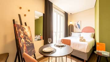 Una habitación de hotel con cama, una mesa de comedor con sillas, un cuadro en la pared y una ventana con cortinas.