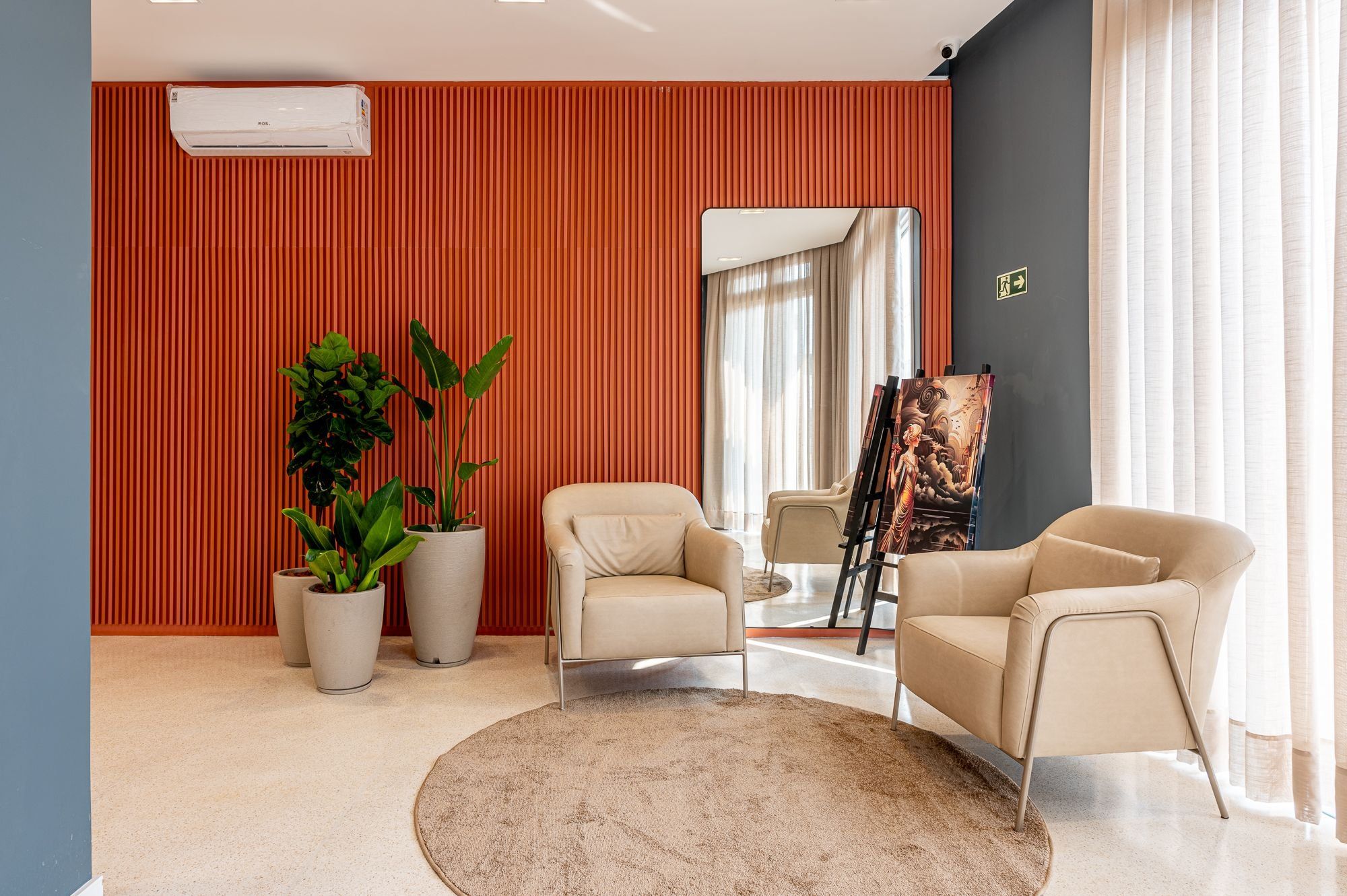 A modern living room with beige sofas, a large potted plant, and a painting on easels.