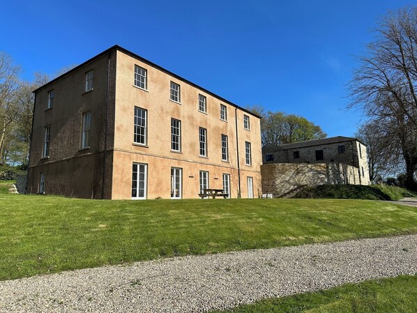 A large, rectangular building with multiple windows and a stone structure adjacent to it. - Captivating 5-bed Apartment Near Sion Mills (Strabane)