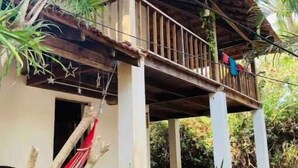 Een rustiek houten huis met rieten dak, een balkon en een hangmat.