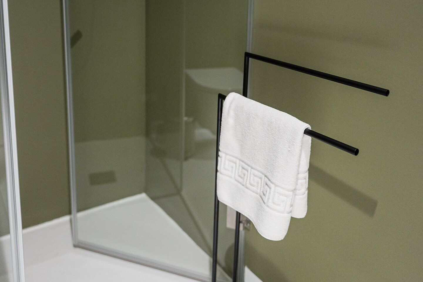 Cabina de ducha de vidrio con una toalla blanca colgada en un perchero negro.
