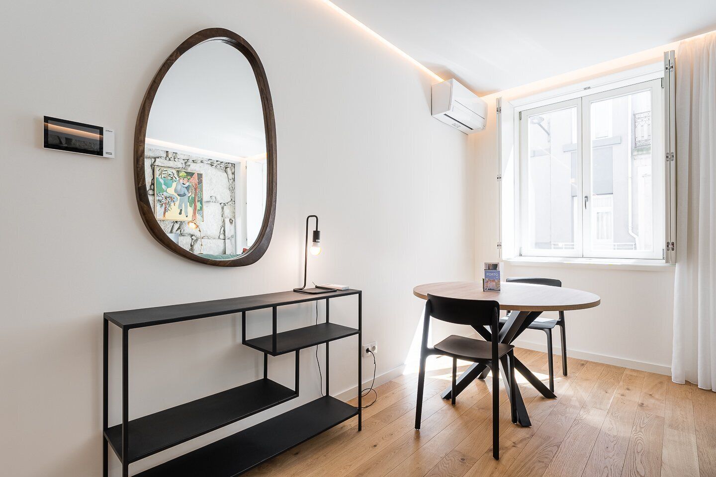 A modern room with a round table, a black console, a large mirror, and a window with curtains.