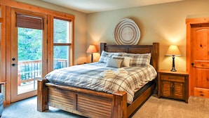 Quarto com cama de madeira, duas mesas de cabeceira com abajures, uma janela grande com persianas e uma porta de madeira.