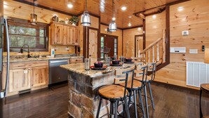 Une cuisine avec des meubles en bois, un plan de travail en granit et un îlot central en pierre agrémenté de tabourets de bar.