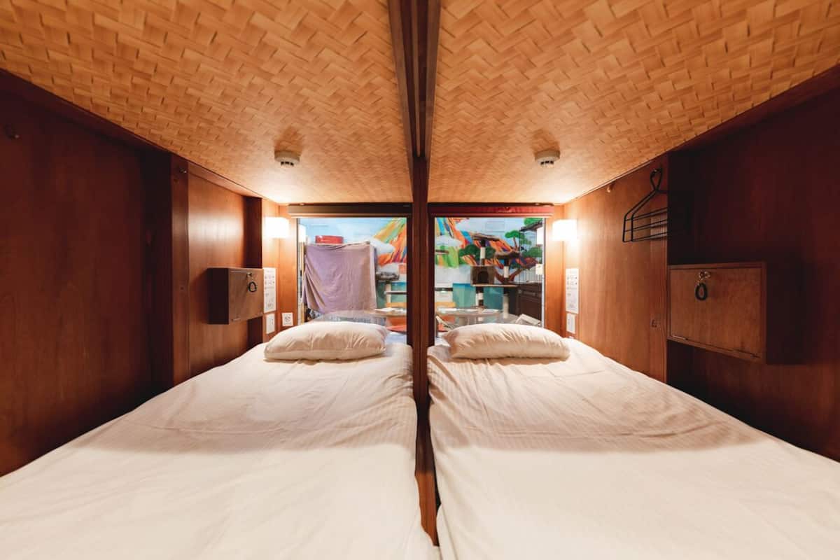 Une pièce aux murs recouverts de miroirs, avec deux lits, des murs en bois et une vue sur un espace extérieur aux couleurs vives.